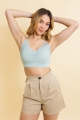 Young woman in blue lace crop top and beige shorts posing with hands behind head